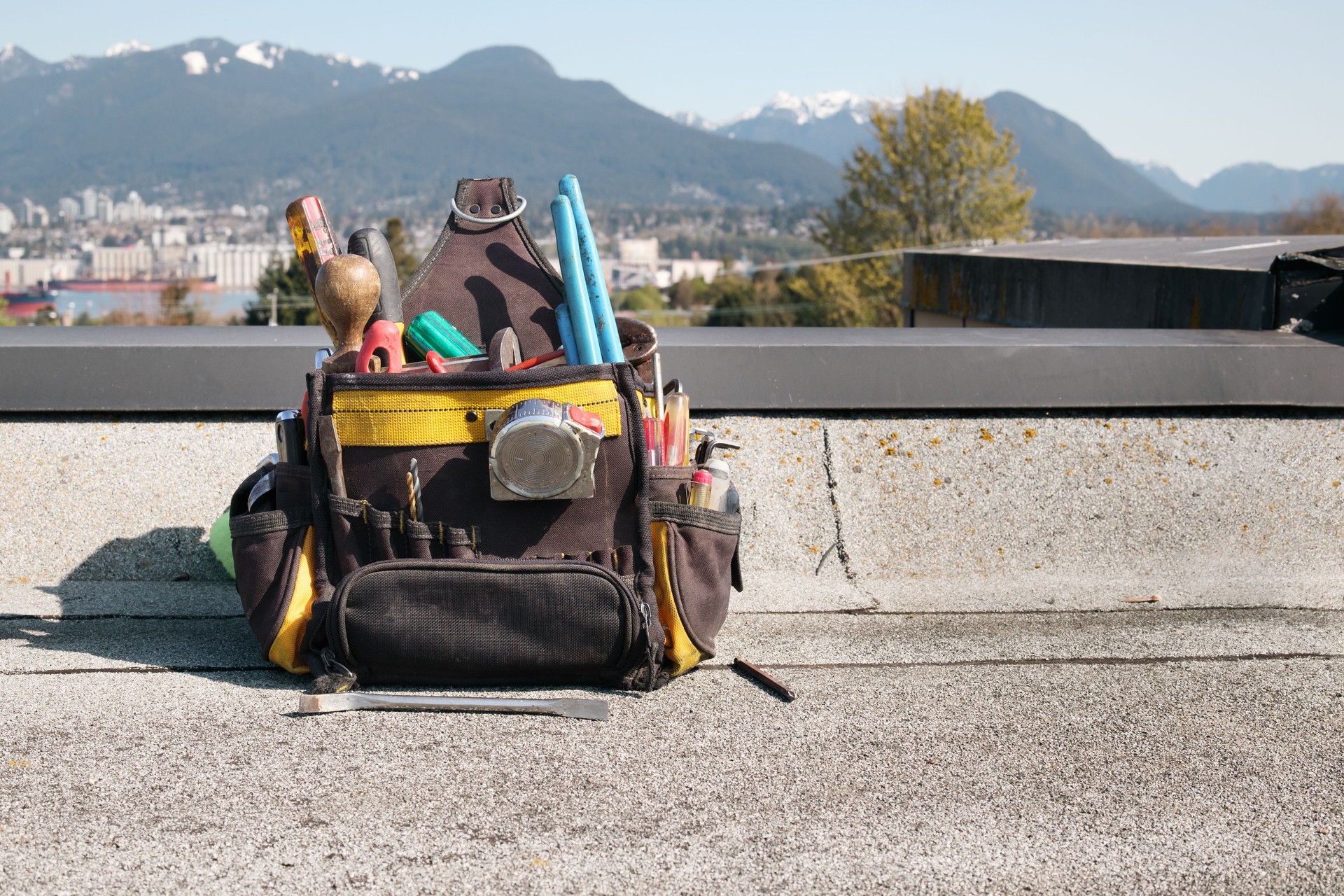 Tool bag or tool kit on roof in front of defocused city skyline and mountains.